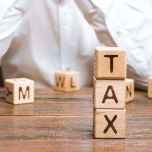 Word "TAX" on wooden blocks with businessman in the background